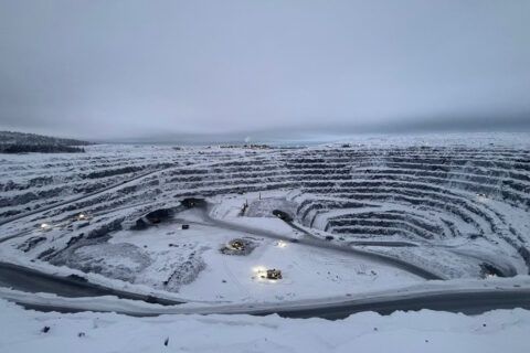 Snötäckt dagbrott med terrasser, vägar och arbetsfordon i vinterlandskap